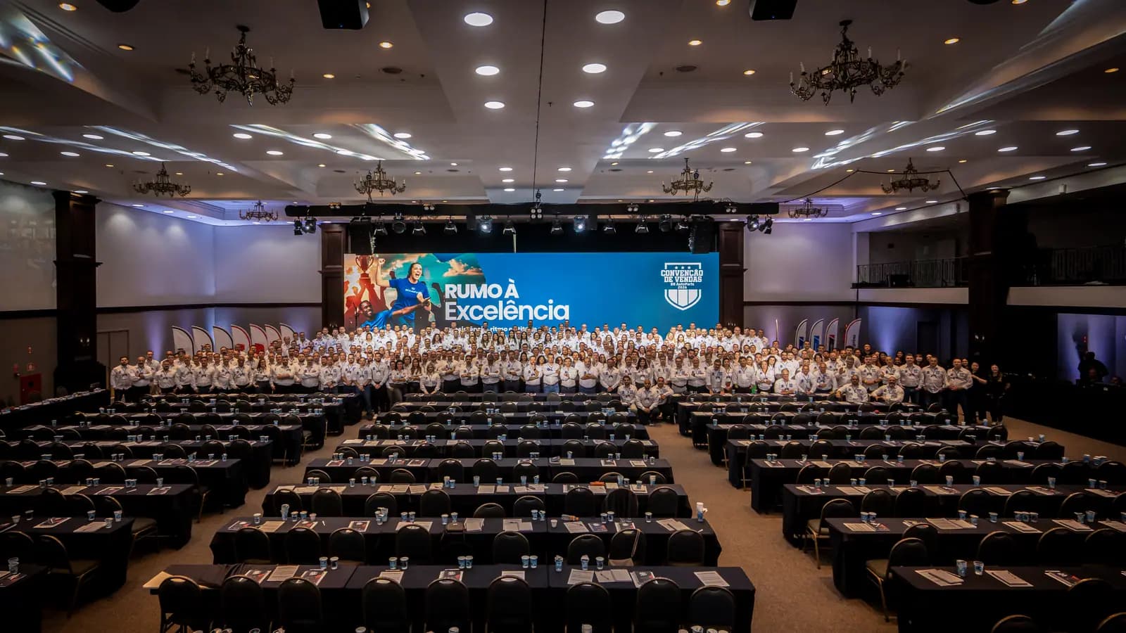 Salão da convenção de vendas visto do fundo, com plateia e telão