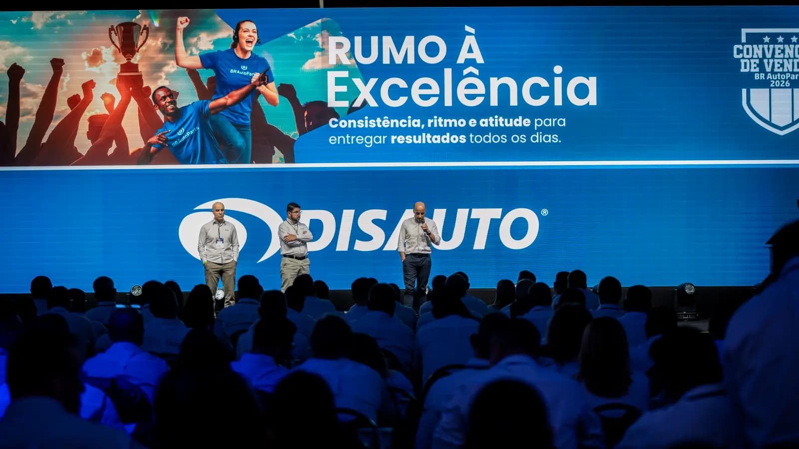 Apresentadores no palco com telão de LED da convenção